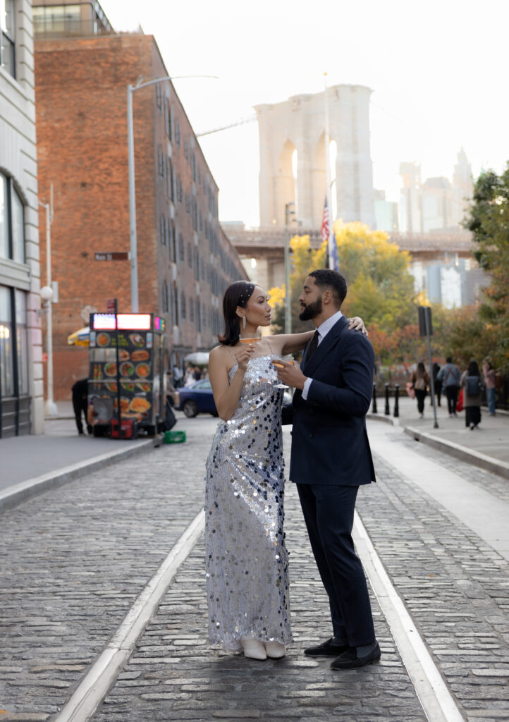 Couple dancing on a cobblestone street in DUMBO, Brooklyn, with the Brooklyn Bridge and city skyline creating a romantic backdrop.