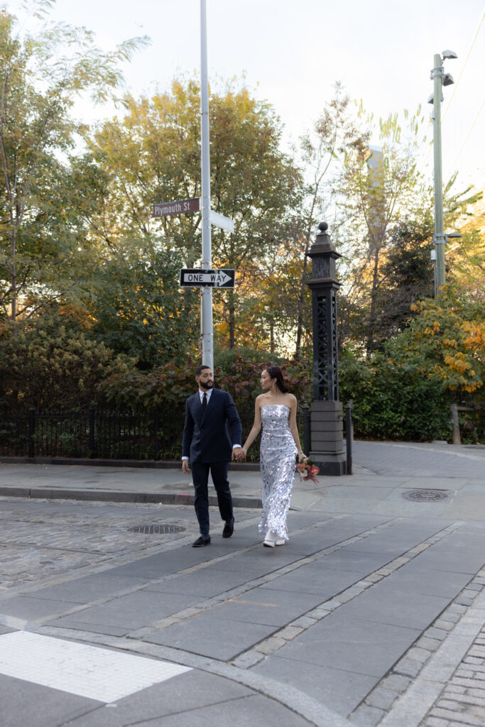 Couple holding hands and walking past the Plymouth Street and One Way signs in DUMBO, surrounded by lush trees and autumn colors.