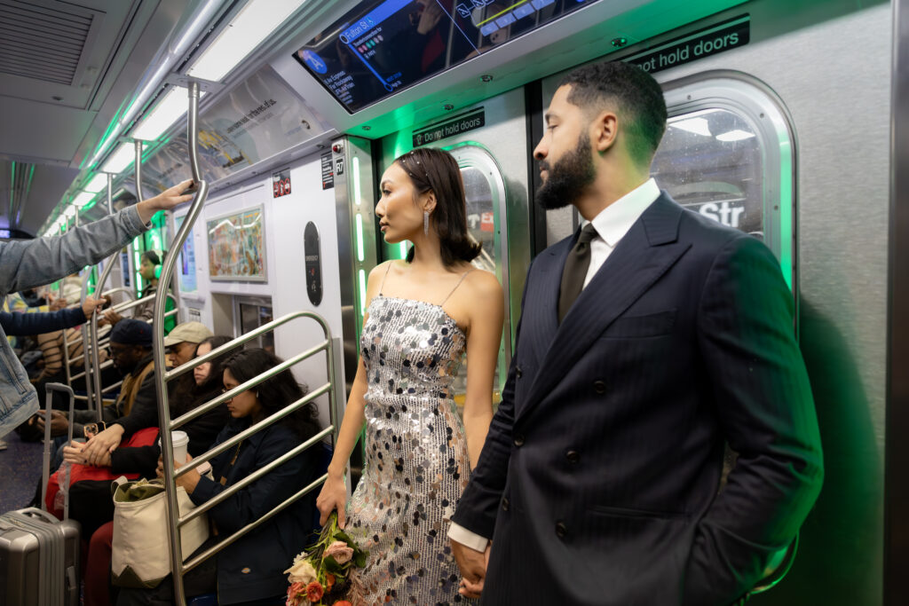 Couple standing inside a New York City subway train, the bride in a sequined dress and the groom in a suit, with soft lighting highlighting their expressions.