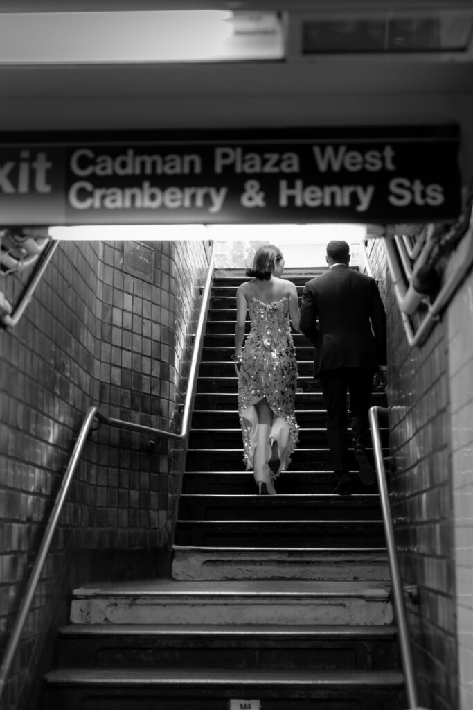 Couple walking up the stairs of the Cadman Plaza West subway exit in Brooklyn, with the bride wearing a sparkling sequined dress and the groom in a dark suit.